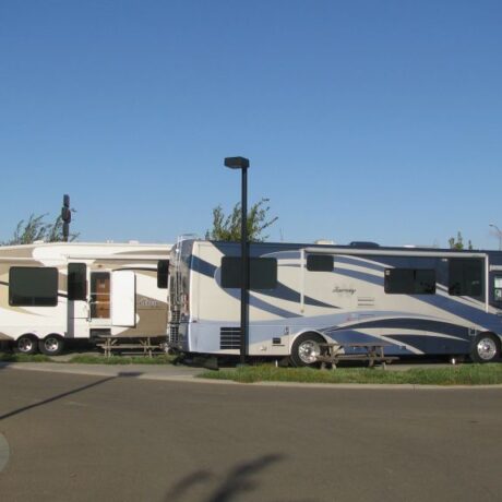 A row of large RVs parked on wide, paved sites at Flag City RV Resort in Lodi, CA.