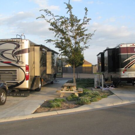 A row of large RVs parked on wide, paved sites at Flag City RV Resort in Lodi, CA.