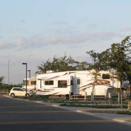 A row of large RVs parked on wide, paved sites at Flag City RV Resort in Lodi, CA.
